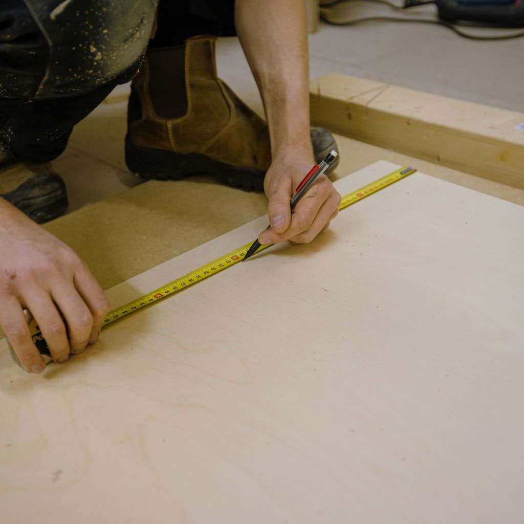Contractor marking a cut line on plywood with a tape measure and pencil