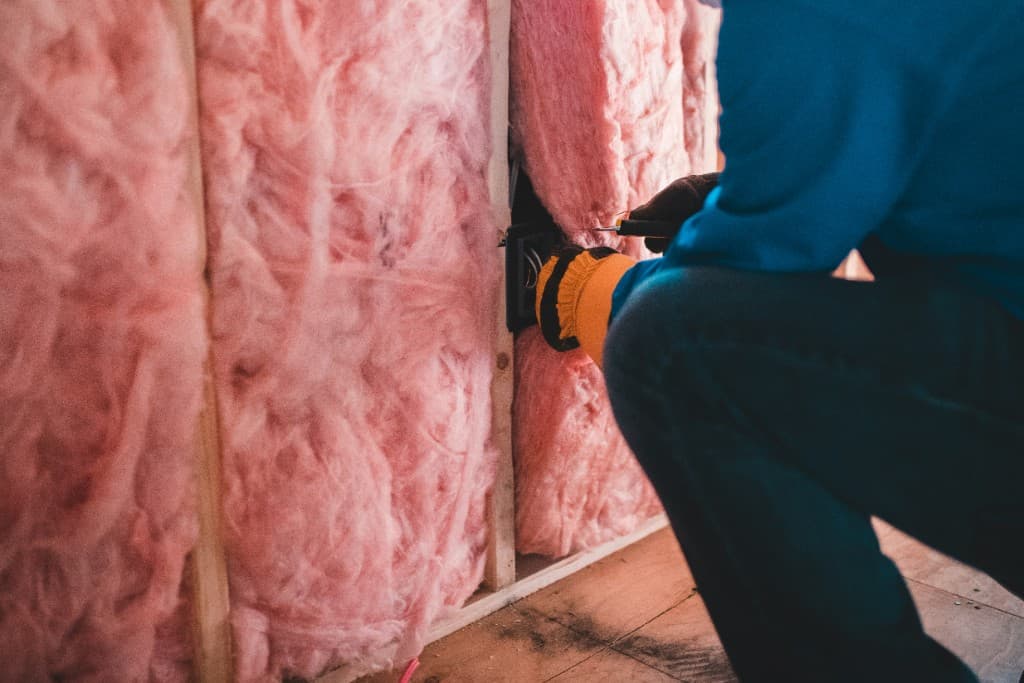 Contractor kneeling beside an open wall with fresh insulation during an interior remodel